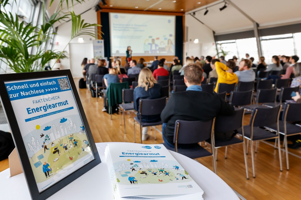 Ein Raum voller Menschen bei der Fachtagung der KEA - der Koordinationsstelle zur Bekämpfung von Energiearmut - in Wien, von der Rückseite weg fotografiert und ein Tisch auf dem Broschüren aufliegen