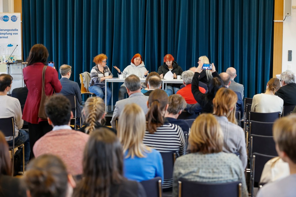 • Energiearmut aus Perspektive von Menschen mit Armutserfahrung –
Theater der Ver-Rückten der Plattform Sichtbar Werden  - diese sitzen am Tisch am Podium, während im Hintergrund Menschen sitzen und zuhören.